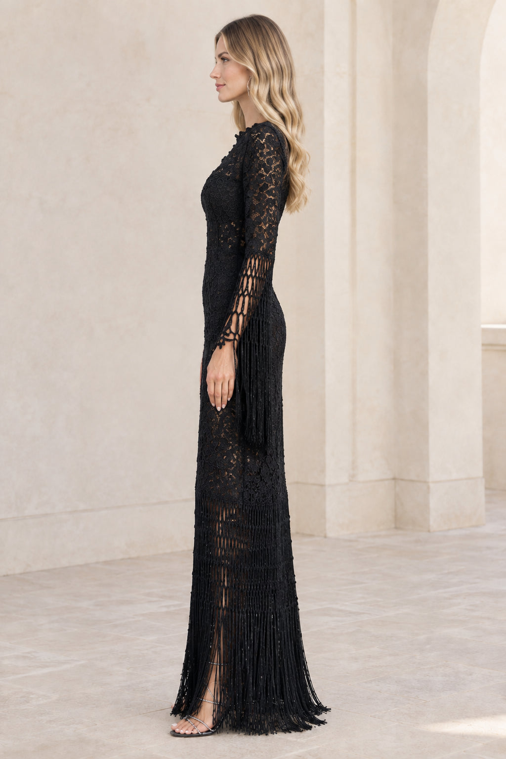 Side profile view of model in black long sleeve lace fringe evening gown