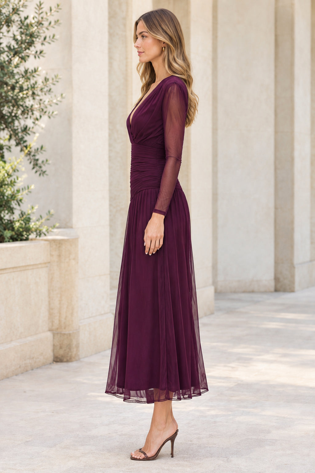 Side angle of woman in plum ruched long sleeve midi evening dress