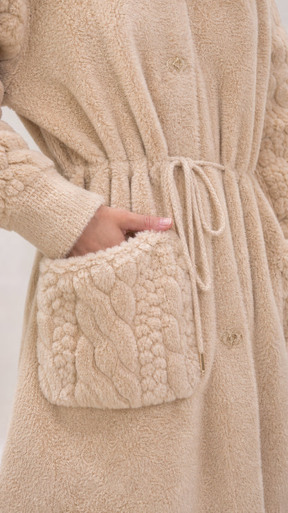 Close-up detail of beige fleece coat showing cable-knit pocket and waist drawstring