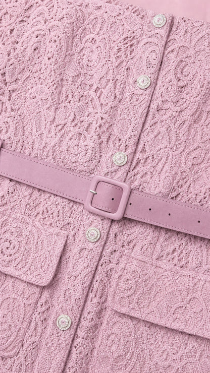 Close-up detail of textured pink lace fabric, decorative buttons, and matching buckle belt